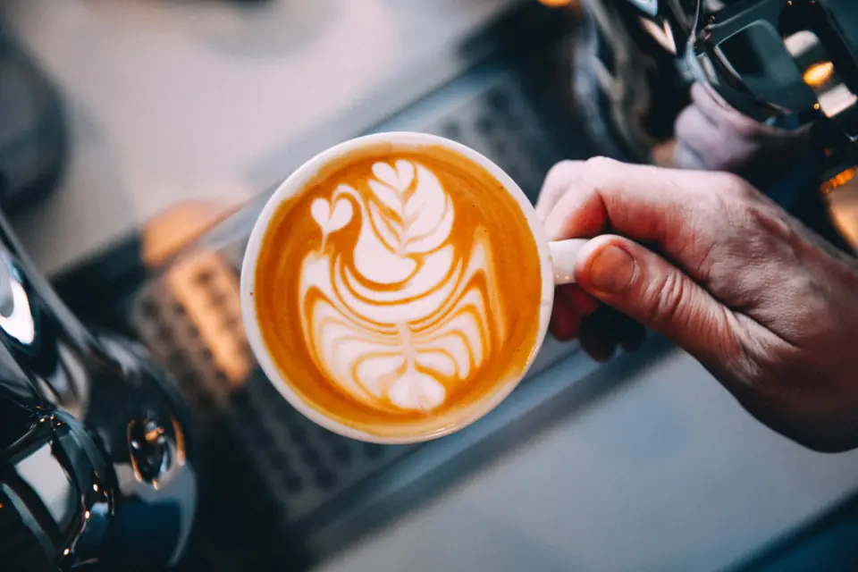 A barista holds up a freshly poured latte next to the espresso machine