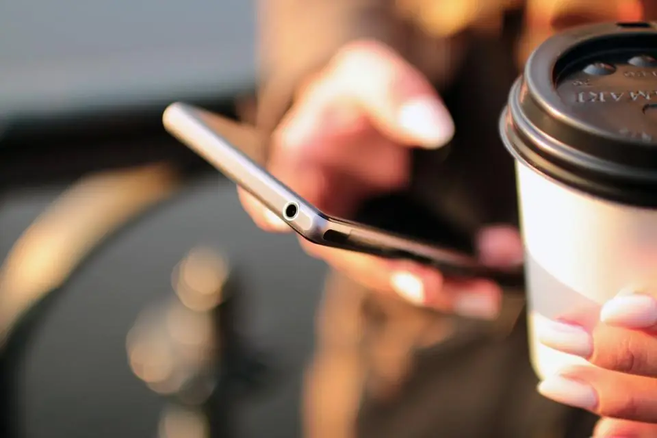 A customer holding a takeaway coffee cup and a smartphone