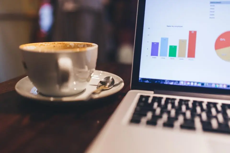 A laptop showing bar and pie charts next to a cup of coffee