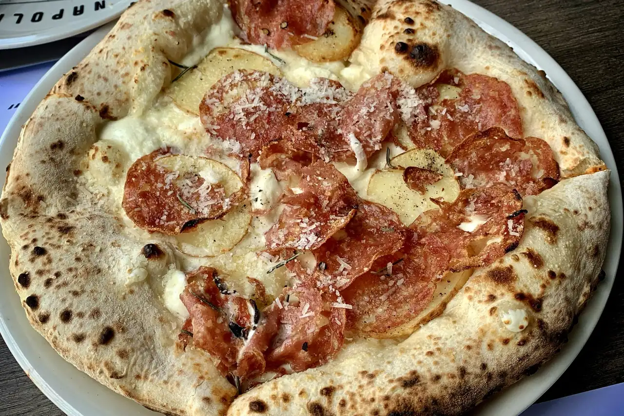 A wood-fired salami pizza served on a restaurant table