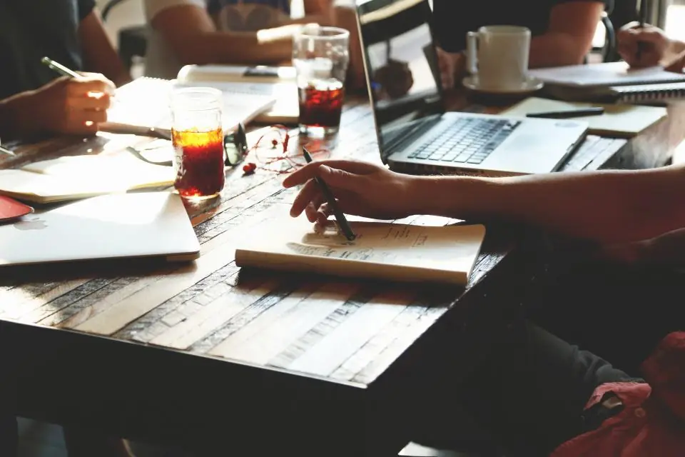 A team around a table with notebooks and laptops, going through their notes