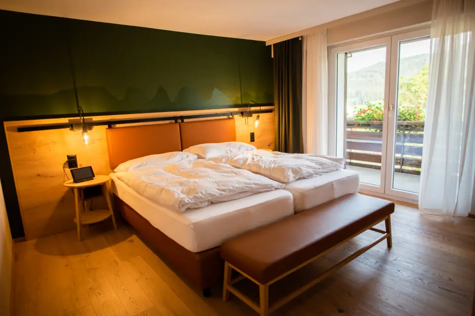 A warmly lit hotel room with a double bed and balcony doors