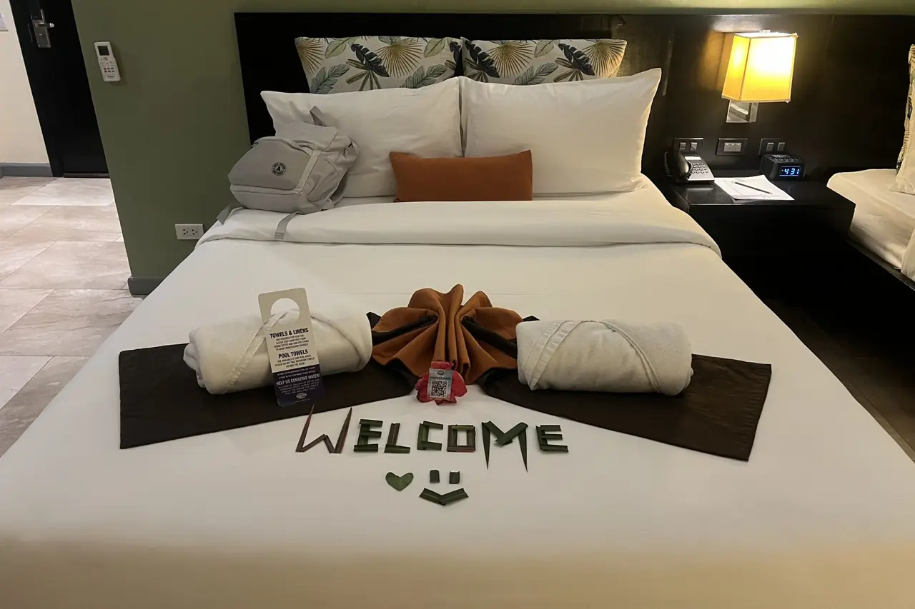 A hotel bed made up for arriving guests, with a welcome message laid out on it